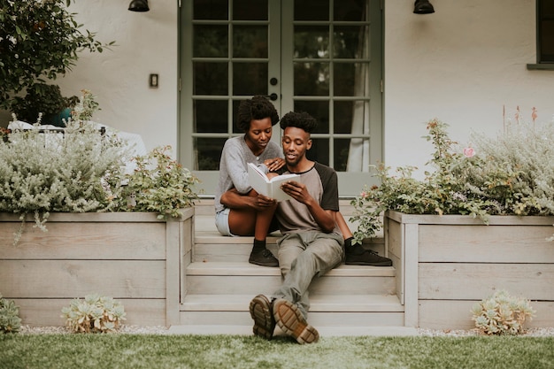 Joli couple noir lisant un livre ensemble dans un jardin