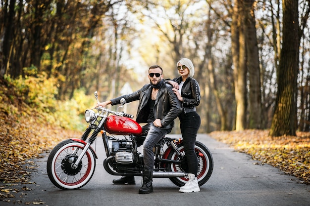 Joli couple près de moto rouge sur la route dans la forêt