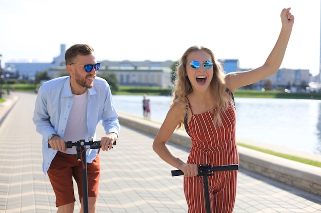 Joli couple s'amusant à conduire un scooter électrique le long de la promenade de la ville.