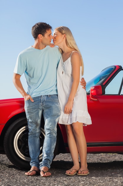 Joli couple s&#39;embrassant contre leur cabriolet rouge