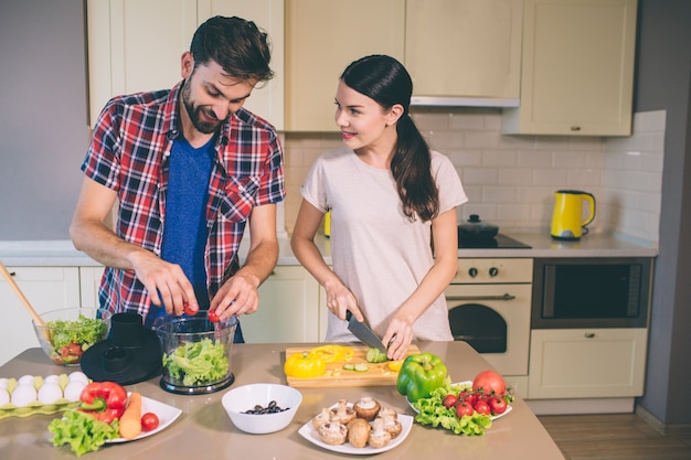 Joli couple travaille ensemble dans la cuisine. Elle coupe les champignons et regarde le gars.