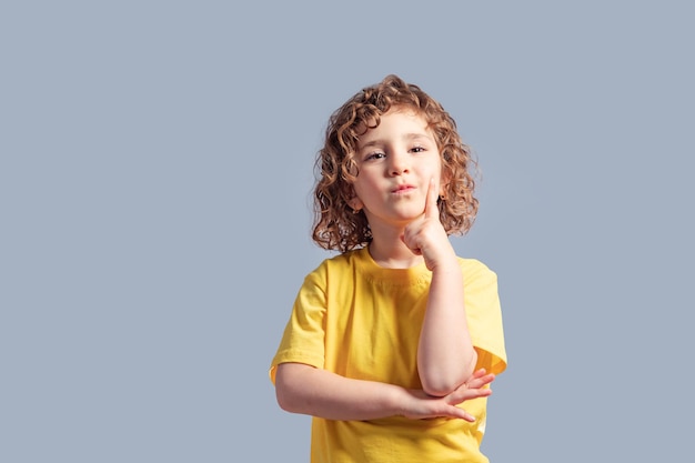 Joli enfant de 5 ans en t-shirt jaune tournant la tête sur le gris