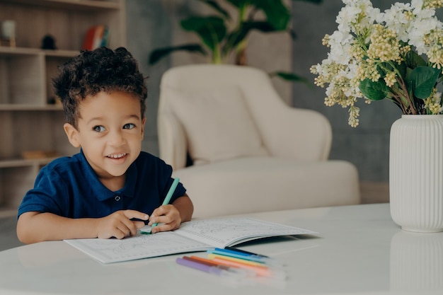 Joli enfant afro-américain peignant dans un livre de coloriage à la maison