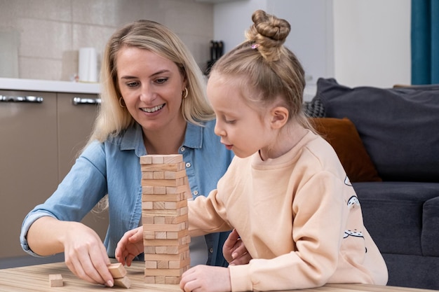 Joli enfant aux cheveux blonds apprenant à construire une tour à partir de blocs de bois jouets à la maison en s'amusant