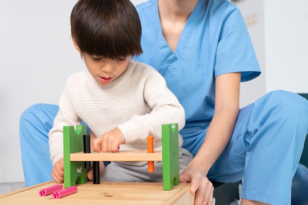 Joli enfant handicapé jouant avec des jouets en développement tout en étant aidé par un physiothérapeute en re...