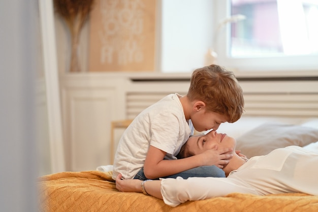 Joli fils et sa charmante maman se touchent le nez et sourient tout en se reposant ensemble sur le lit