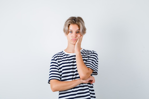 Joli garçon ado penché sur la joue en t-shirt rayé et ayant l'air de s'ennuyer. vue de face.