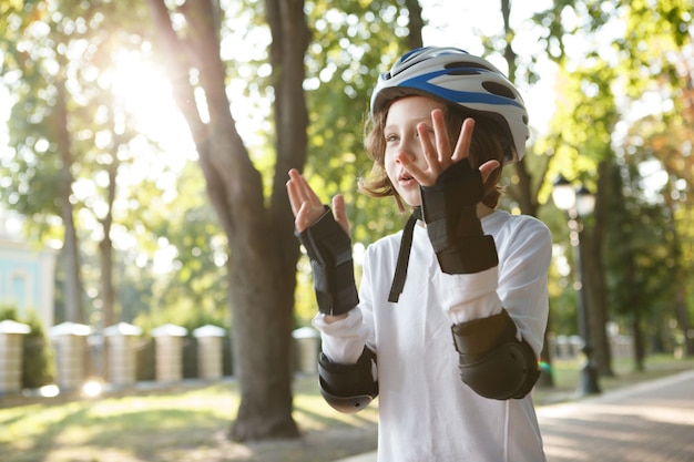 Joli garçon appréciant le patinage dans le parc, portant un équipement de protection en patins à roues alignées