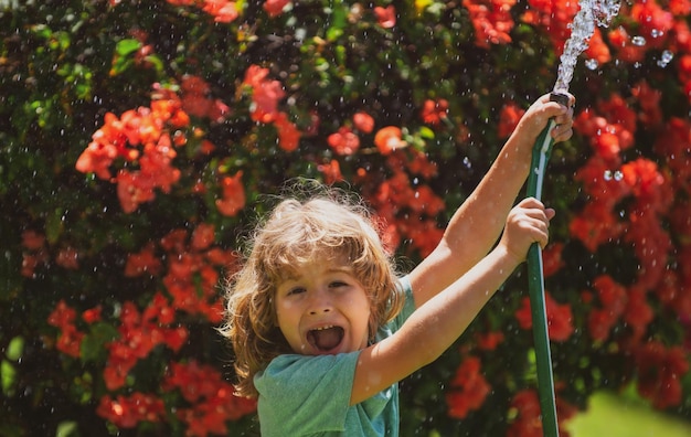 Joli garçon arrosant des plantes dans le jardin le jour d'été Enfant avec des outils de jardin et un tuyau d'arrosage dans le jardin de l'arrière-cour Enfant s'amusant sur la cour Le concept de gentillesse et d'enfance des enfants