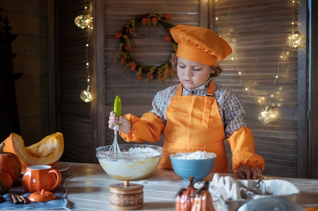 Un joli garçon aux cheveux bouclés dans un costume de chef orange prépare une tarte à la citrouille pour Thanksgiving. traditions de vacances en famille