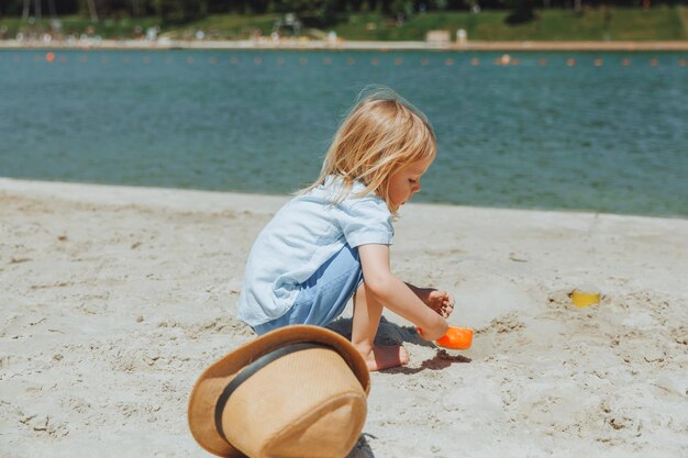 Joli garçon blond heureux jouant avec des jouets de plage sur la plage de sable de la ville