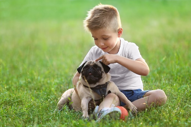 Joli garçon avec chien carlin sur l'herbe verte