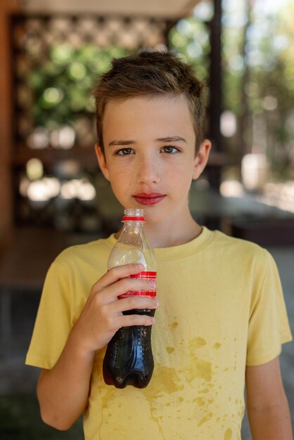 Un joli garçon dans un T-shirt jaune tient une bouteille à la main et en boit de la limonade Chaleur estivale