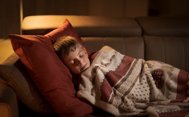 Joli garçon dormant sur le canapé à la maison sous une couverture douce