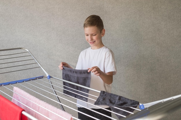 Joli garçon faisant des tâches ménagères accrochant des vêtements mouillés sur le sèche-linge