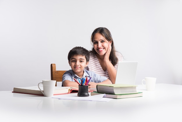 Joli Garçon Indien Avec Sa Mère Faisant Ses Devoirs à La Maison à L'aide D'un Ordinateur Portable Et De Livres - Concept De Scolarisation En Ligne