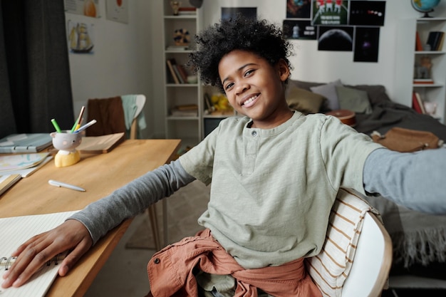 Photo joli garçon souriant en tenue décontractée vous regardant assis près du bureau