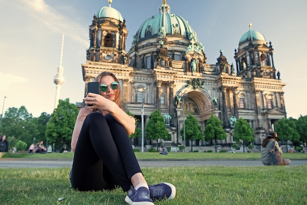 Joli gil assis devant la cathédrale de Berlin au beau coucher de soleil et faisant un selfie