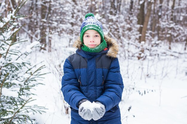 Joli jeune garçon joue avec la neige, s'amuse, sourit. Adolescent dans le parc d'hiver. Mode de vie actif, hiver
