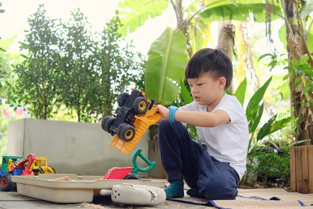 Joli jeune garçon de la maternelle asiatique jouant avec du sable et des machines de construction de jouets seul à la maison