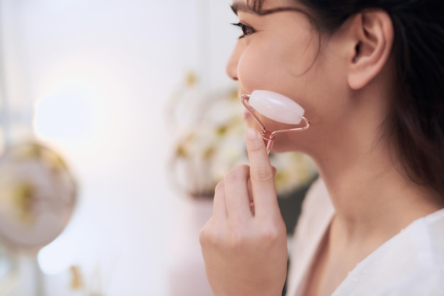 Joli modèle utilisant un rouleau de pierre cosmétique pour le massage du visage.
