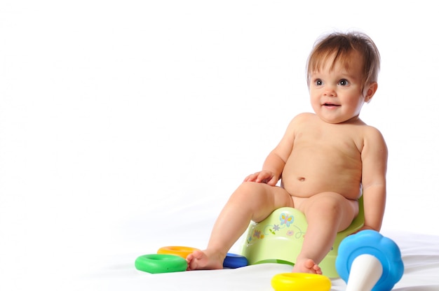 Photo joli petit bébé est assis sur un pot vert et joue au jouet aimé.