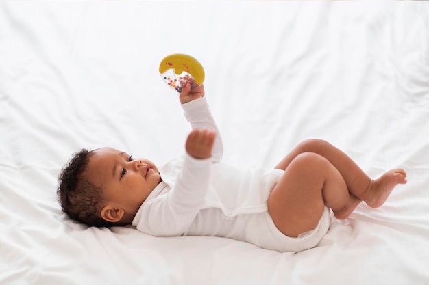 Photo joli petit bébé noir avec jouet hochet à la main relaxant au lit