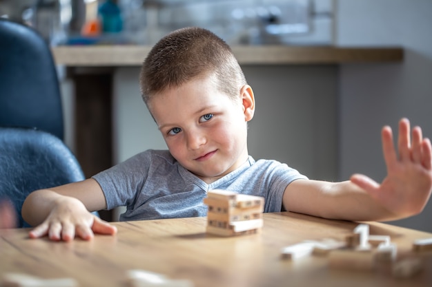 Un joli petit garçon joue à un jeu de société avec des cubes en bois et une tourelle.