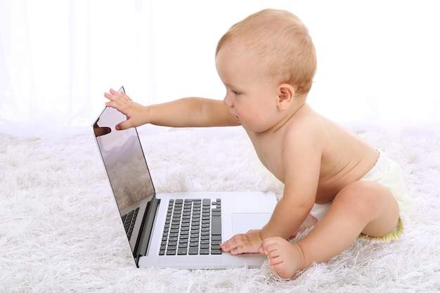 Photo joli petit garçon avec un ordinateur portable sur un tapis dans la chambre