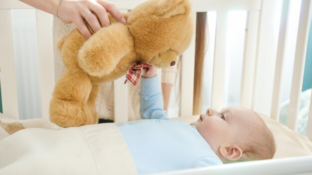 Photo joli petit garçon regardant un ours en peluche tenu par la mère concept de bonheur familial parental et de développement du bébé