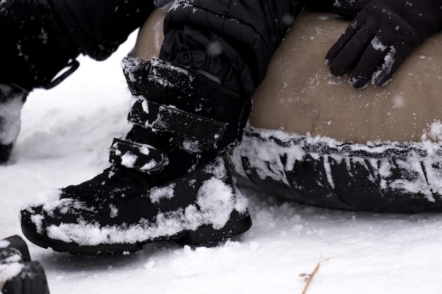 Un joli petit garçon en salopette sombre glisse sur une glissade de glace, des jeux d'enfants d'hiver, un enfant dans un parc en hiver. Petit garçon s'amusant d'hiver extrême sur des tubes