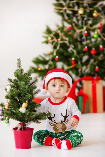 Joli petit père Noël en pyjama blanc et vert. Sapin de Noël et cadeaux du nouvel an sur le