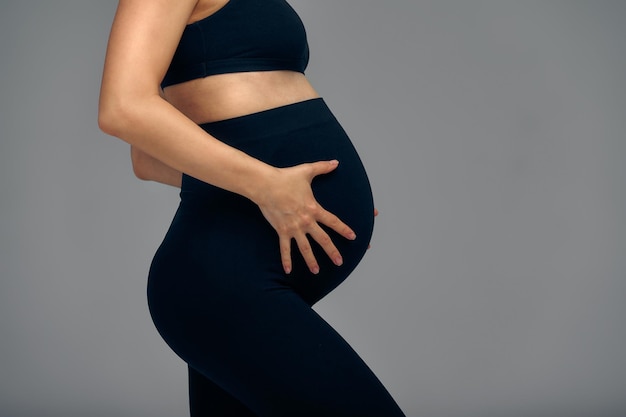 Joli ventre de femme enceinte isolé sur gris Vue latérale d'une jeune femme enceinte embrassant son abdomen avec les mains Gros ventre au troisième trimestre de la grossesse agrandi Concept de vie enceinte