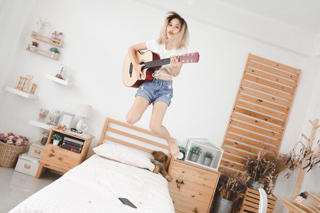 Joli visage de femme asiatique J'ai beaucoup aimé elle joue de la guitare et a sauté sur son lit Heureux indépendant complètement se détendre se détendre avec un problème