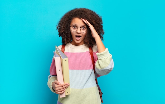 Jolie adolescente afro à l'air heureuse, étonnée et surprise, souriante et réalisant une bonne nouvelle incroyable et incroyable. concept d'étudiant