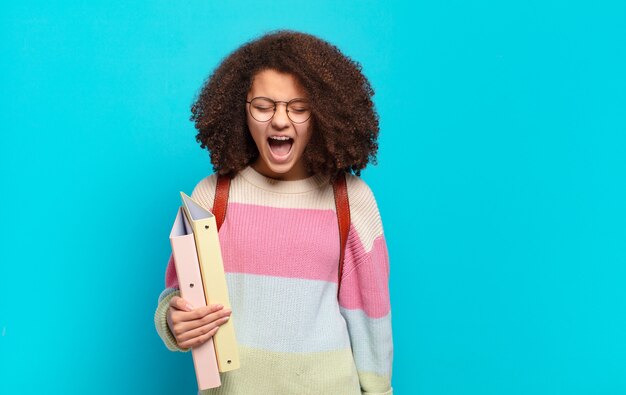 Jolie adolescente afro criant de manière agressive, l'air très en colère, frustrée, indignée ou agacée, criant non. concept étudiant