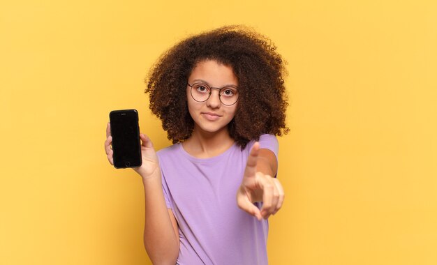 Photo jolie adolescente afro souriant fièrement et avec confiance en faisant la pose du numéro un triomphalement, se sentant comme un leader et tenant une cellule