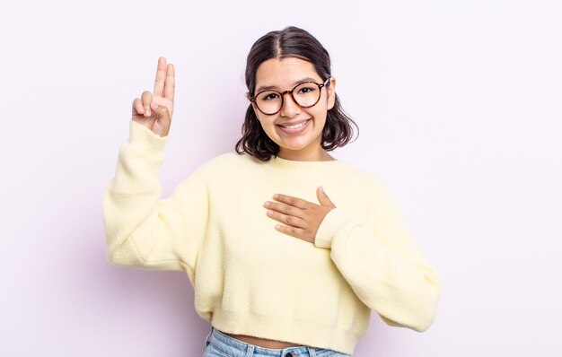 Jolie adolescente à l'air heureuse, confiante et digne de confiance, souriante et montrant le signe de la victoire, avec une attitude positive