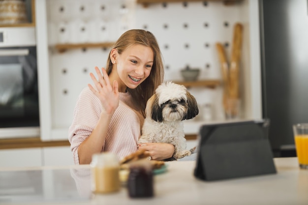 Une jolie adolescente assise avec son mignon chien et passant un appel vidéo sur une tablette numérique chez elle.