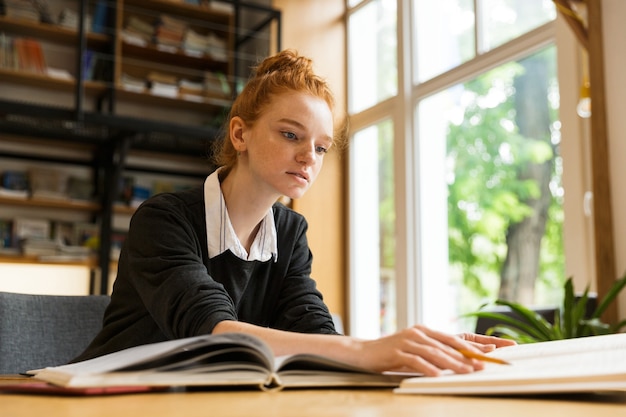 Jolie adolescente aux cheveux rouges étudie à la table