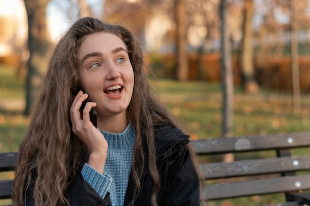 Jolie adolescente aux longs cheveux bruns dans le parc parlant émotionnellement au téléphone