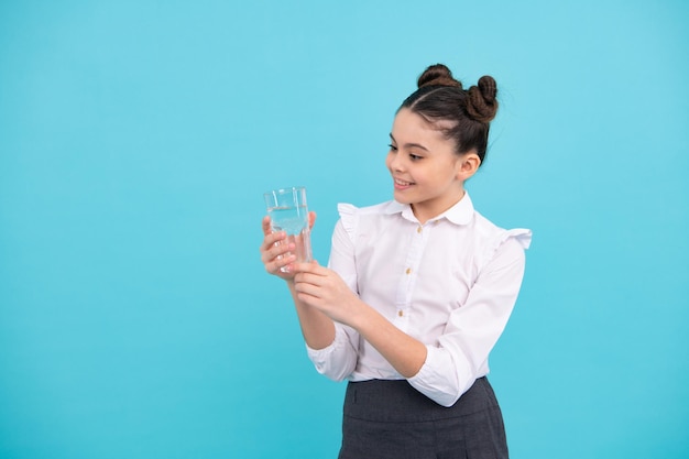 Jolie adolescente buvant de l'eau à partir de verre sur fond bleu Heureux adolescent émotions positives et souriantes d'une adolescente