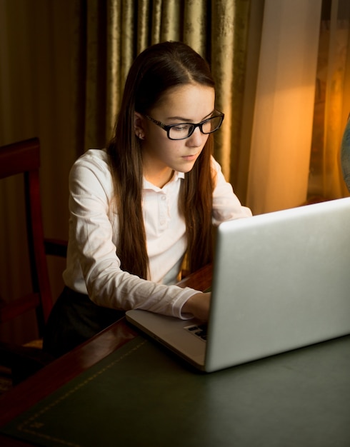 Jolie adolescente en chemise blanche en tapant un message sur ordinateur