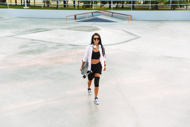 Jolie adolescente funky exerçant son longboard en marchant au skatepark