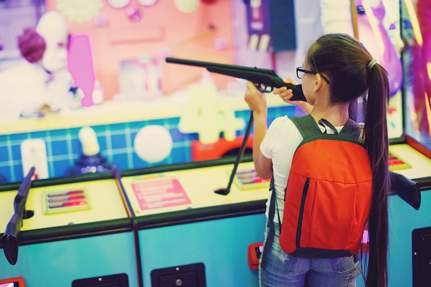 Une jolie adolescente joue un fusil d'arcade dans une machine de jeu dans un parc d'attractions.