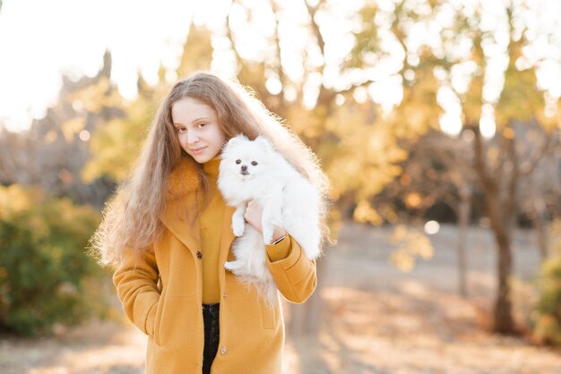 Jolie adolescente souriante de 15 à 16 ans tenant un chiot spitz blanc moelleux ensemble au cours de l'automne