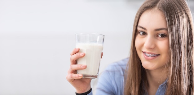 Une jolie adolescente souriante avec un appareil dentaire tient un verre de lait frais