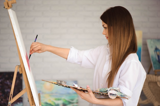 Jolie artiste belle fille peindre une image sur une toile sur un chevalet.