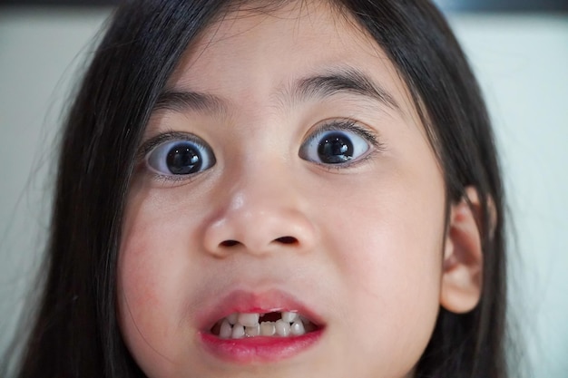 Une jolie asiatique aux gros yeux fait des grimaces avec ses dents de lait qui tombent