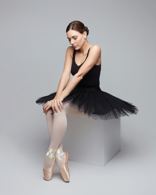 Jolie ballerine pose gracieusement assise sur un cube. séance photo en studio sur fond blanc